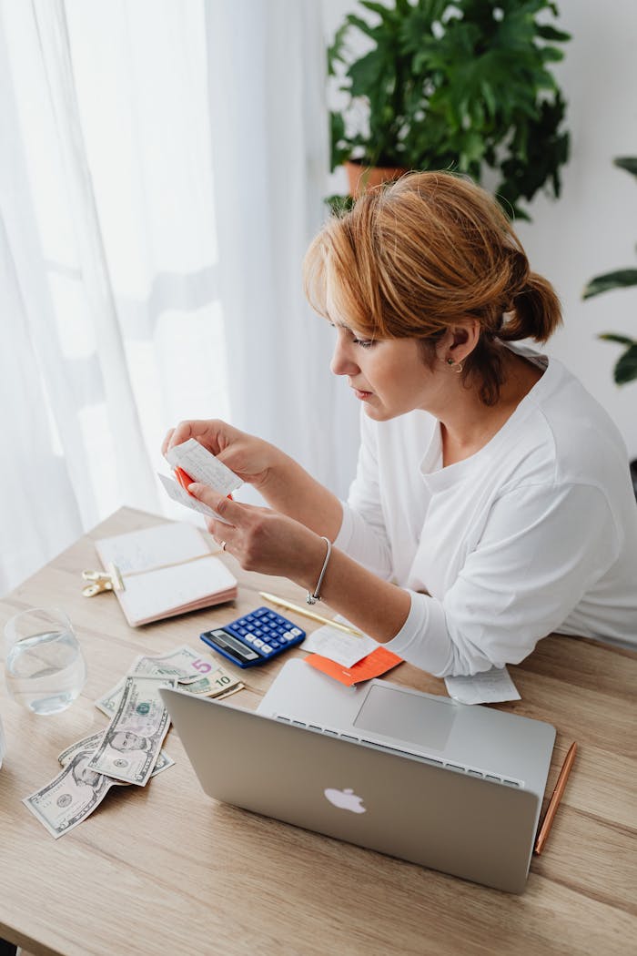 Woman calculating budget with laptop, cash, and receipts at desk.